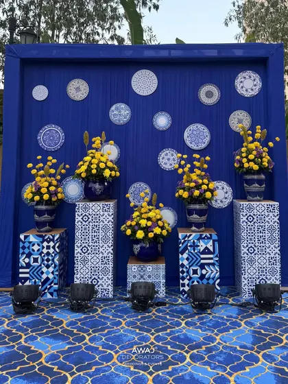 A photo-op backdrop with a wall of decorative plates and vibrant floral arrangements in matching blue and white vases.