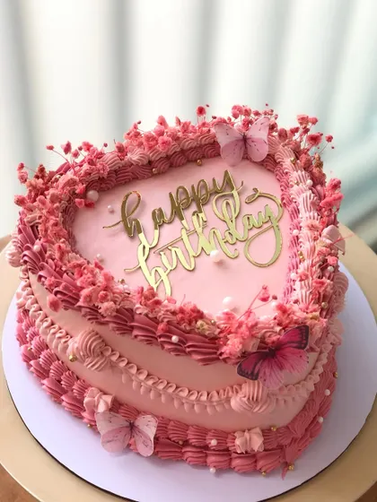A heart-shaped vintage-style cake in shades of pink, decorated with dried flowers and edible butterflies.