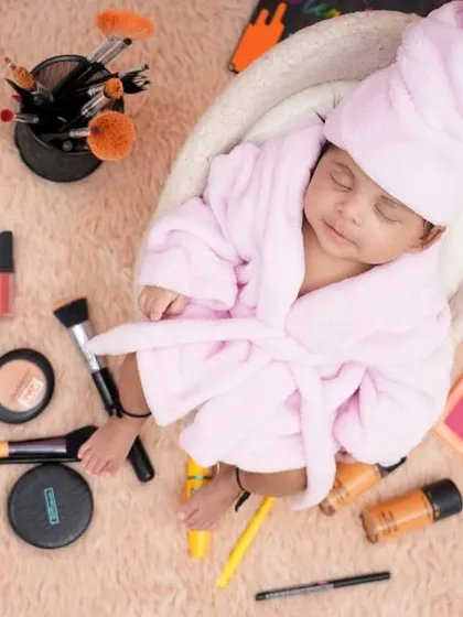 A close-up of a sleeping newborn in a pink robe, surrounded by makeup accessories. This themed shoot is a fun way to add a unique and humorous twist to your baby's first portraits.
