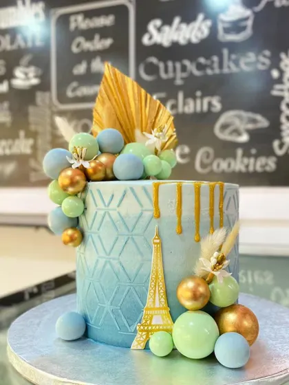 A closer studio shot of the Paris-themed cake, highlighting the intricate details of the gold drip, geometric texture, and decorative spheres.