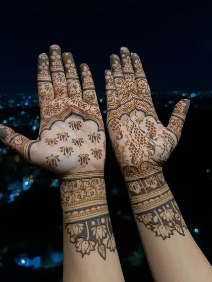 A beautiful mehendi design with a cityscape in the background. The palms feature a mix of peacock and floral motifs, with bold lotus bands on the wrists.