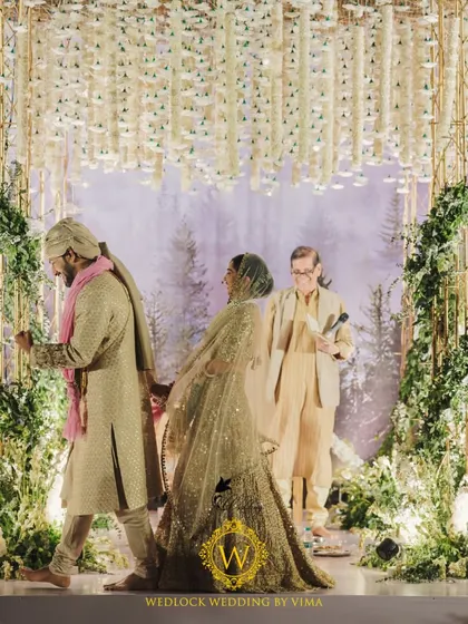 A candid moment from a beautiful minimalist wedding. The couple is framed by the modern mandap, which features a canopy of white florals against a backdrop of a misty forest.