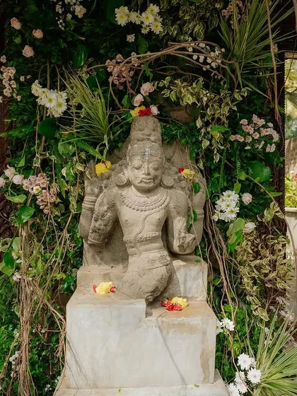 A stone deity statue adorned with flowers, a spiritual and beautiful focal point for a wedding ceremony.