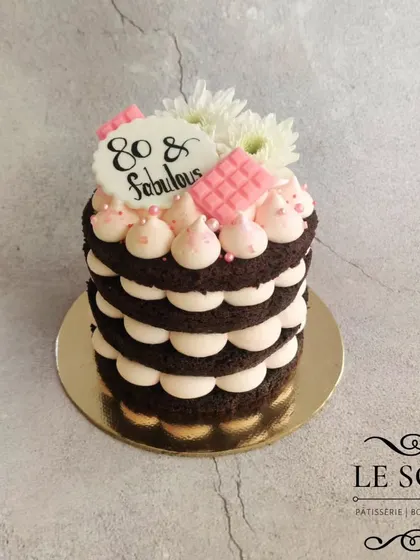 A semi-naked cake for an 80th birthday. This half-kg chocolate cake is layered with pink-tinted cream cheese frosting and decorated with ruby chocolate and fresh flowers.