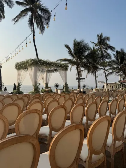 A view of the guest seating facing the sea, with the elegant white mandap as the focal point. The string lights add a touch of warmth to the open-air setting.