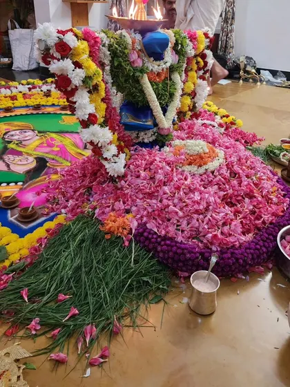 A kalasha decorated with a blue saree and flowers, placed on a rangoli.