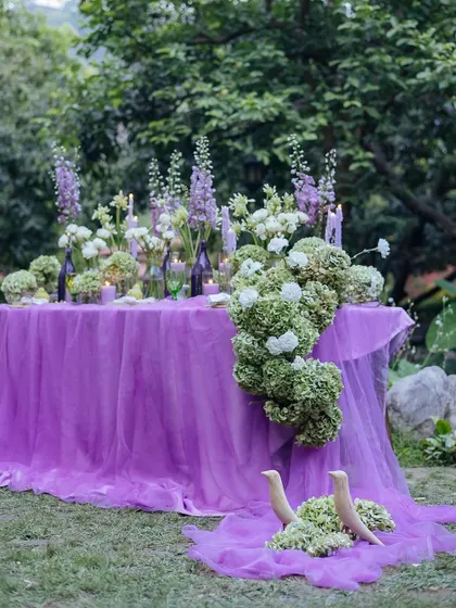 A wide shot of the beautifully decorated table, with a flowing purple runner and an abundance of flowers.