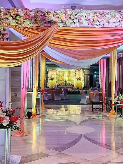 A beautiful entrance decoration at The Suryaa Hotel. The hallway is transformed with draped arches in peach and white fabric, accented with lush floral arrangements.
