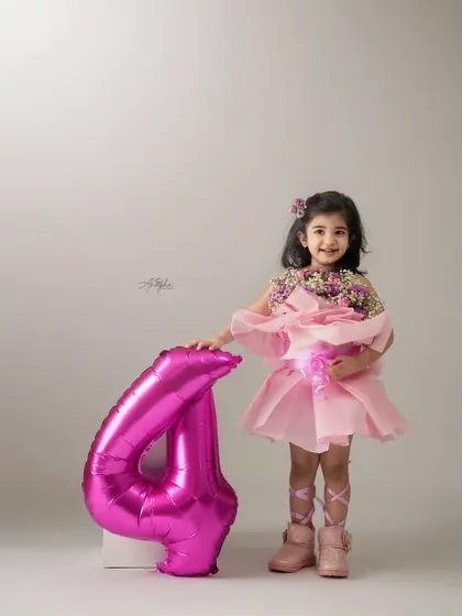 Celebrating turning four with a pretty pink theme. This little girl is dressed like a ballerina, holding a bouquet, next to a large number '4' balloon.