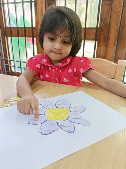 A young girl carefully places pieces of paper to create a flower mosaic. This paper art activity helps develop fine motor skills and patience.