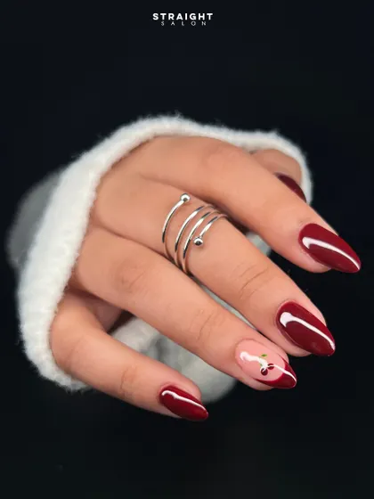 A classic deep red manicure with a playful twist. I hand-painted a delicate cherry design on a negative space accent nail for a touch of sweetness.
