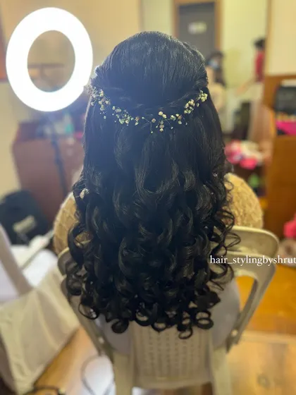 A half-up style with tight, bouncy curls, accessorized with a delicate garland of baby's breath. This look is romantic and perfect for an outdoor or daytime event.