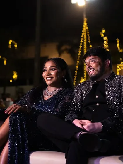 The couple enjoys the Sangeet performances, their faces lit by the stage lights and happiness.