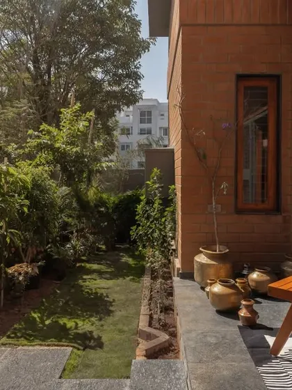 The 'ಜಗಲಿ' (jagali), or deck, is a sun-soaked space designed for relaxation, connecting the home's interior with the lush garden.