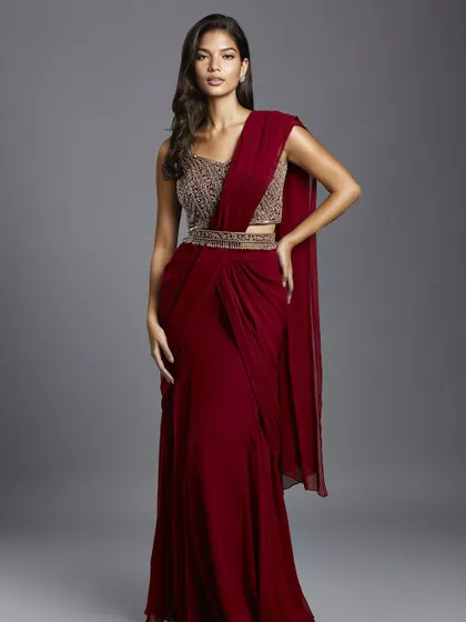 A stunning maroon draped saree with a heavily embellished blouse and belt, a glamorous choice for a reception or cocktail party.