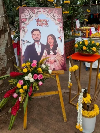 A custom welcome sign for Hamza and Ifrah's Mehendi, featuring their caricature and surrounded by vibrant floral arrangements that match the event's decor.