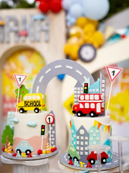 All aboard the party bus! These two adorable cakes are from a "Wheels on the Bus" themed party, featuring a school bus and a double-decker bus, complete with road signs and cityscapes.