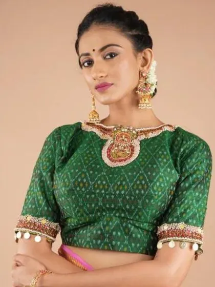 A model wears a green Ikat blouse with a heavily embellished neckline, paired with large traditional jhumkas.