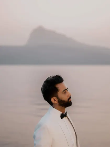 A classic portrait of the groom, Himanshu, set against the calm water and distant mountains at dusk. The soft, ambient light is perfect for capturing pensive and elegant shots.