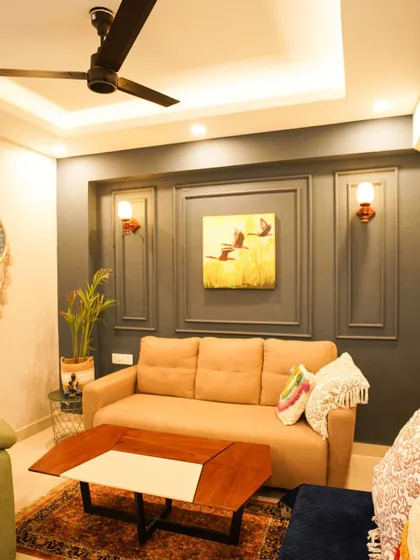 A comfortable living room with a neutral color palette, featuring a plush beige sofa against a dark grey accent wall with classic wainscoting. This design choice adds depth and character to the space.