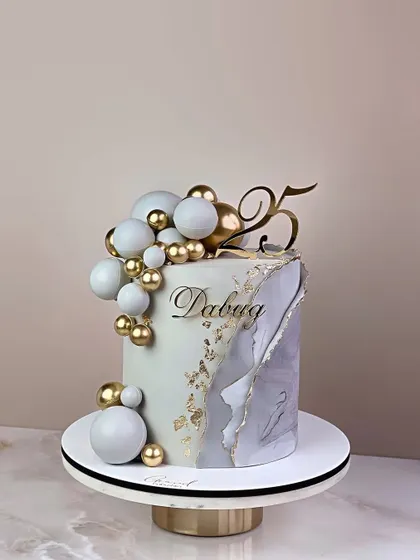 An elegant 25th celebration cake with a marble effect, torn-edge gold leaf, and a cascade of white and gold spheres.