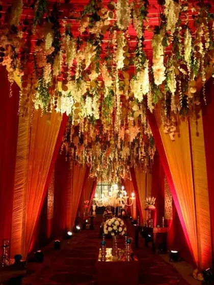 A grand wedding entrance tunnel draped in rich red and gold fabrics, with a ceiling of cascading flowers, creating a royal welcome.