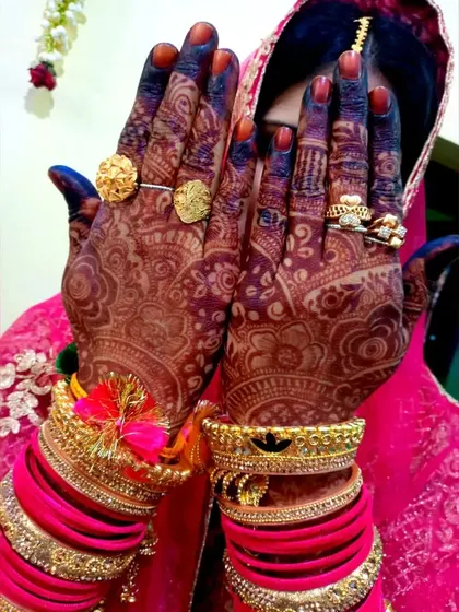 A beautiful candid shot of a bride, her face hidden behind her hands, showcasing the stunningly dark henna stain against her vibrant pink wedding attire.