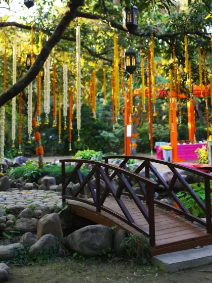 The picturesque setting for a Mehendi at Taj Corbett, with a wooden bridge and trees adorned with hanging flower garlands.