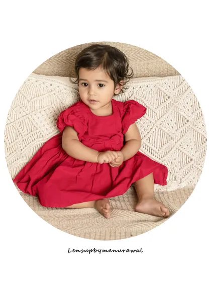 A beautiful, simple portrait of a toddler in a lovely red dress, sitting thoughtfully on a textured blanket in a circular frame, highlighting her innocent expression.