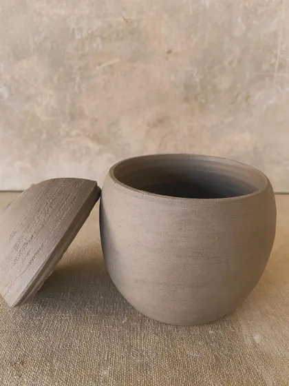 This unglazed lidded jar has a slightly curved lid, giving it a soft, gentle silhouette. It's a perfect example of wabi-sabi beauty.
