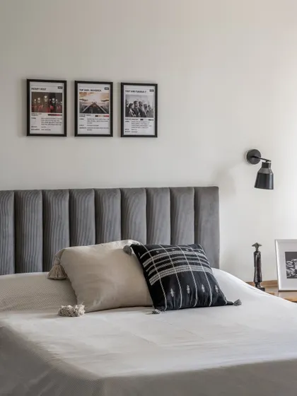 A simple yet stylish bedroom design featuring a channeled headboard in grey velvet and a gallery of minimalist movie posters. The black and white theme creates a modern, graphic look.