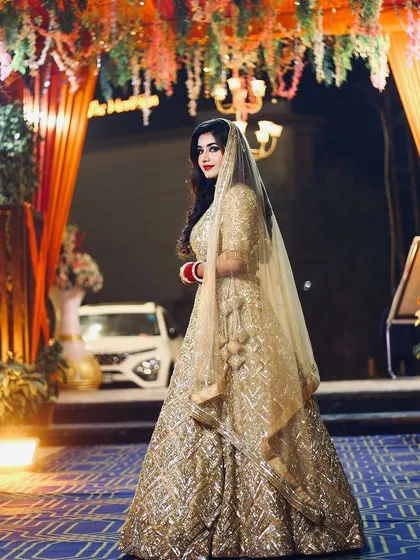 A full-length shot of the reception bride at the venue. The golden lehenga and glowing makeup look magnificent under the lights.