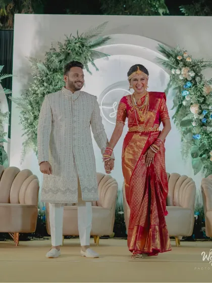 The couple shares a happy moment on their elegant reception stage, featuring modern curved backdrops, soft lounge seating, and delicate floral arrangements.