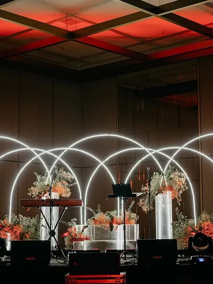 We designed this stunning stage for a live band performance at a reception, using intersecting neon arches and floral arrangements to create a vibrant and contemporary look.