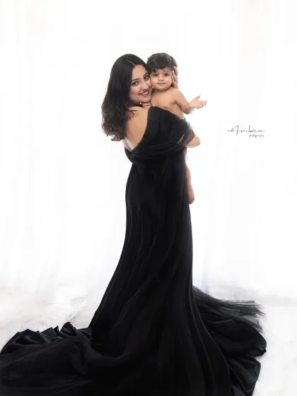 A beautiful mother and child portrait in a dramatic black gown. The high-contrast lighting creates a striking, fine-art image that emphasizes their connection.