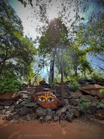A creative and spiritual art installation on a rock at the ecovillage, with a painted face and sun rays filtering through the trees.