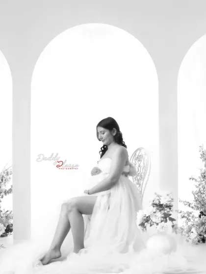 A dreamy black and white portrait of an expectant mother with angel wings. Seated on a bed of clouds, this image has a magical and ethereal quality.