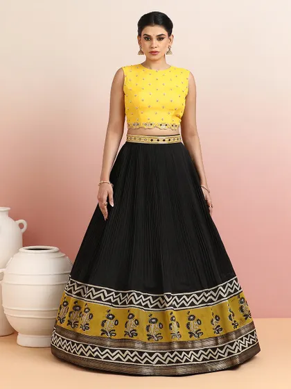 The vibrant yellow blouse radiates festive charm, whether paired with this black pleated lehenga or our metallic paisley skirt.