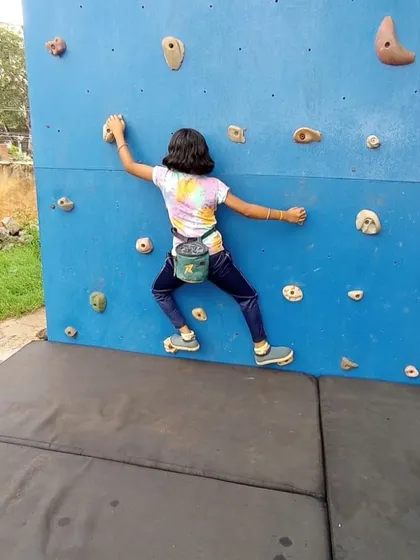 A young boulderer with her chalk bag tackles a problem on the lower section of the wall.
