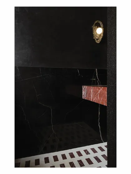 Another view of the dramatic powder toilet. The design highlights the contrast between the veined red marble of the monolith basin and the dark, textured walls, lit by a single, sculptural wall light.