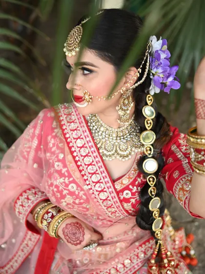 A side profile showcasing the complete bridal look. The hairstyle is adorned with flowers and a mirror-work braid accessory that complements the heavy Kundan jewellery set.