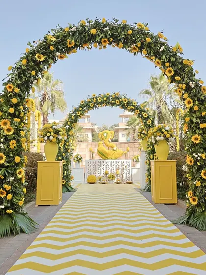 A grand entrance for a sunflower-themed Haldi. The massive floral arches made of sunflowers and greenery, paired with a chevron-patterned aisle, create an impressive and cheerful welcome for guests.