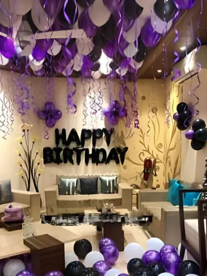 A stylish birthday room decoration with purple and black balloons. The ceiling is covered with balloons, and 'Happy Birthday' foil letters are on the wall.
