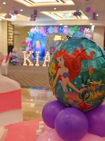 A close-up of a table centerpiece for a Little Mermaid themed party. An Ariel foil balloon sits atop a pink and purple balloon arrangement.