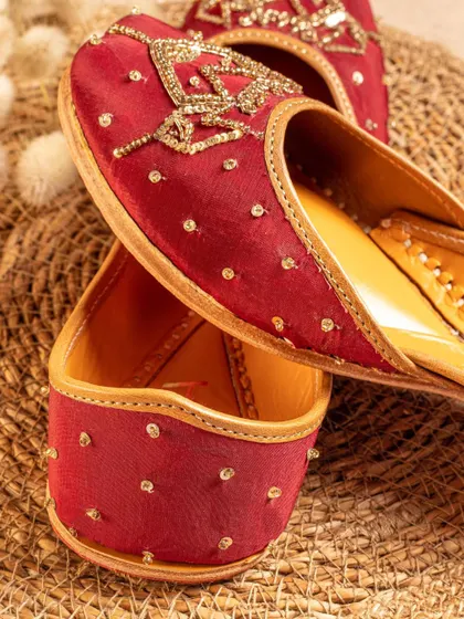 A rich, maroon jutti styled on a textured, neutral background. We carefully select props and backdrops that complement the product without distracting from it.