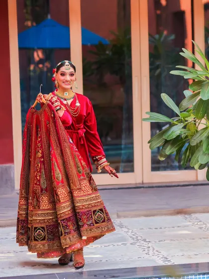 A fun and stylish shot of the bride holding up her wedding lehenga before getting dressed. Her personalized velvet robe adds a modern and personal touch.