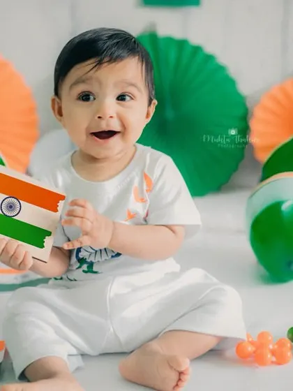 Holding a card with the Indian flag, this baby looks at the camera with a sweet and happy face. The tricolor props create a lively and colorful setting.