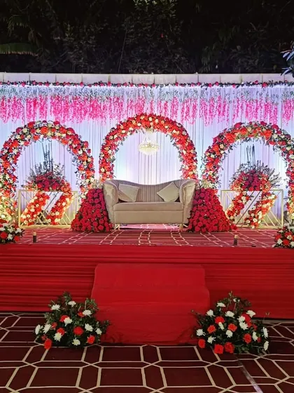 A spectacular stage for a reception, featuring three large floral arches in red and white. The elevated platform and elegant sofa create a grand and regal setting for the couple.