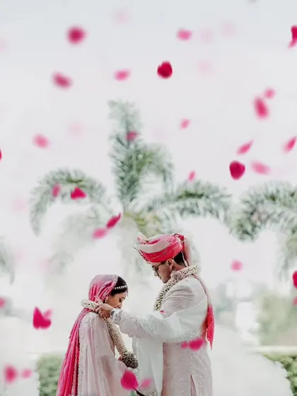 The couple exchanges garlands amidst a cloud of smoke and falling petals, creating a dreamy and romantic atmosphere.