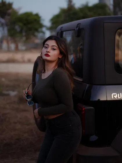 A portrait of a model posing with a Thar jeep at dusk. The soft lighting and her confident pose create a moody and stylish image.